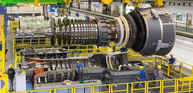 Engineers in hard hats assembling a large gas turbine rotor in an industrial hall
